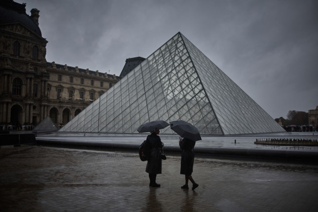Rain-Leaks-Into-Louvres-Cimabue-Exhibition.jpg Two people shelter under an umbrella during a rainy day next to a glass pyramid structure.