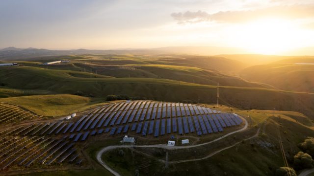 US-solar-keeps-surging-generating-more-power-than-hydro-in.jpg A view of a hlltop lit by the rising sun, with solar panels covering it.