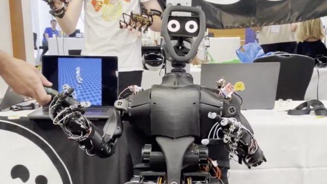 Want-a-humanoid-open-source-robot-for-just-3000-Hugging.jpg A humanoid robot sits in a chair, with a telepresence operator behind it