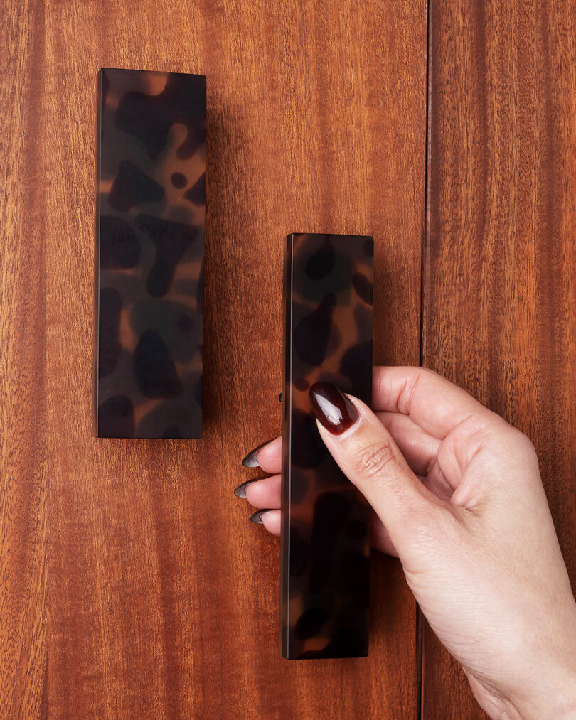 A hand holding a rectangular object with a tortoiseshell pattern next to another similar object on a wooden surface