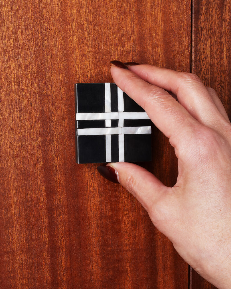 A hand holds a small black knob with a white cross pattern on its surface, positioned against a wooden background