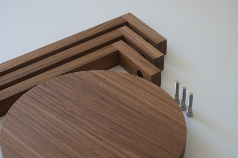 Disassembled wooden table components with three rectangular legs, one circular top, and four metal screws on a white surface