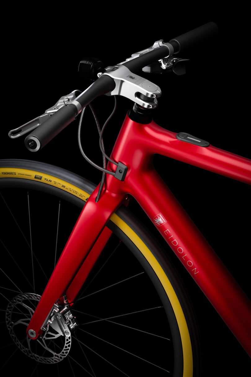 Close-up of a sleek, modern red bicycle frame with black handlebars and yellow-accented wheels against a black background.