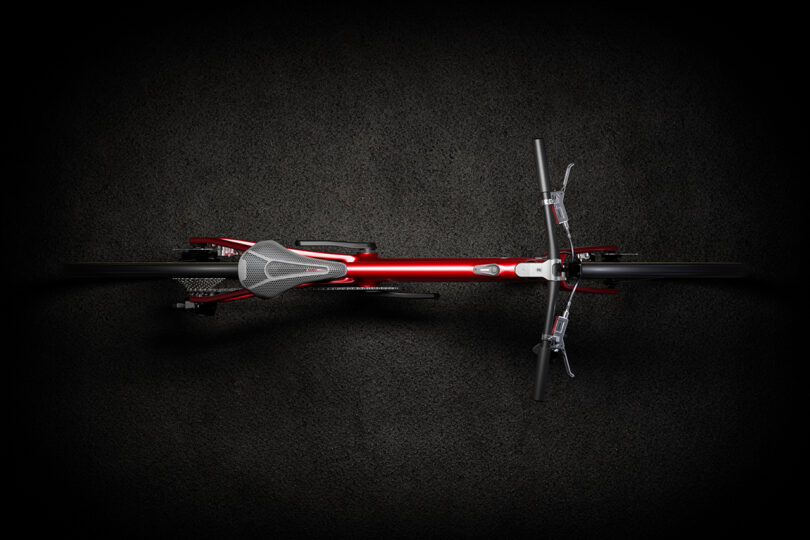 Top view of a sleek, red bicycle with narrow tires, black handlebars, and aerodynamic design against a dark background.