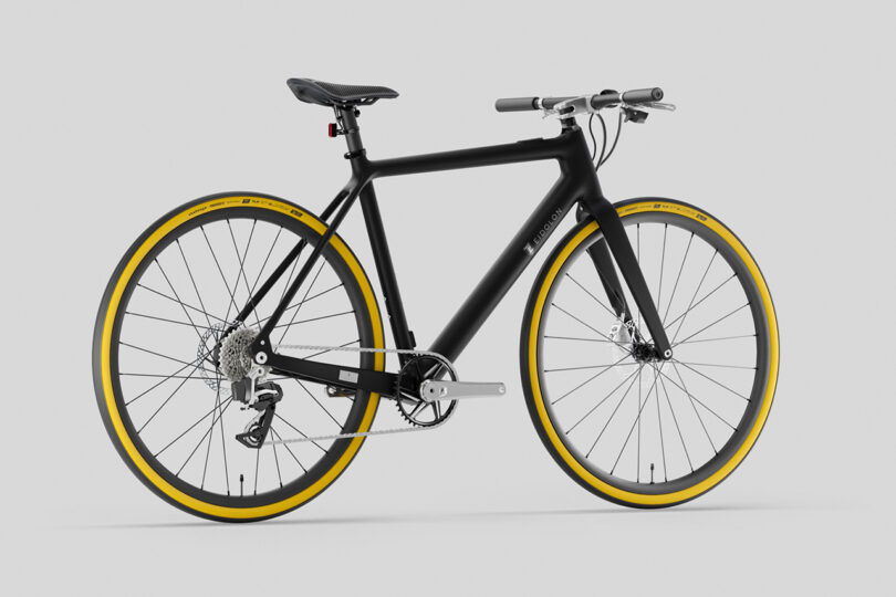 Black bicycle with a sleek frame and yellow-accented tires on a plain gray background.