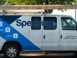 A parked van used by a Spectrum cable technician. The van has the Spectrum logo on its side and a ladder stowed on the roof.