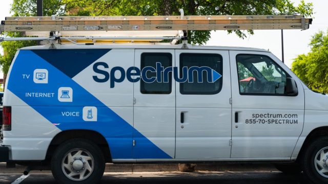 1750178943_Vandals-cut-fiber-optic-lines-causing-outage-for-Spectrum-Internet-subscribers.jpg A parked van used by a Spectrum cable technician. The van has the Spectrum logo on its side and a ladder stowed on the roof.