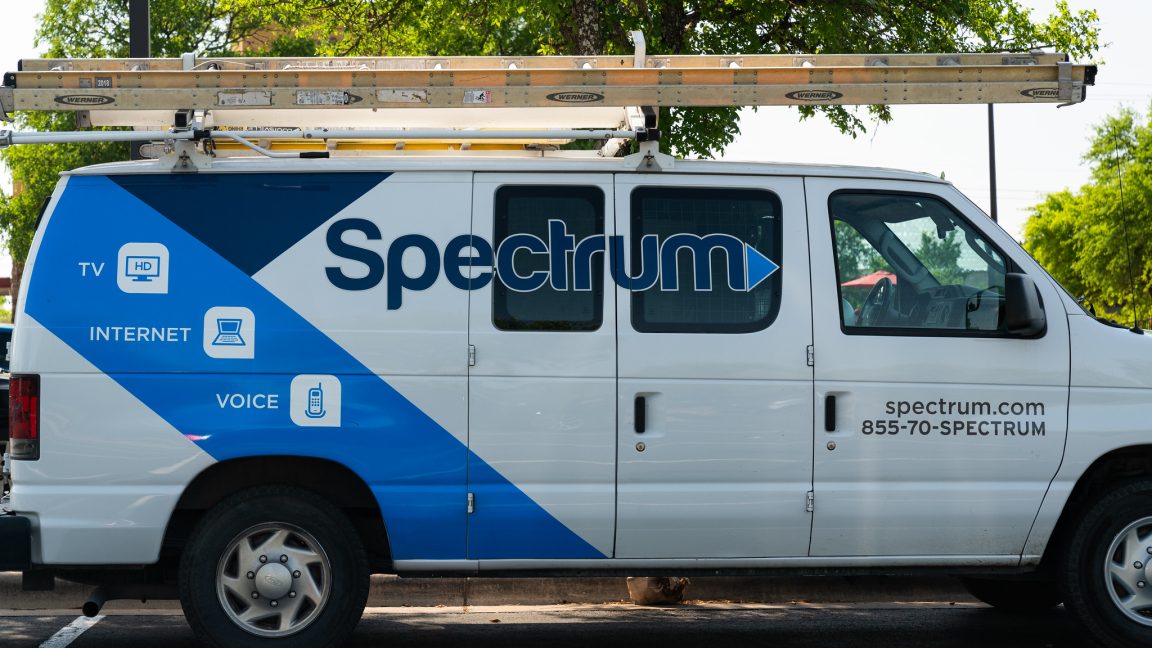 1750178943_Vandals-cut-fiber-optic-lines-causing-outage-for-Spectrum-Internet-subscribers.jpg A parked van used by a Spectrum cable technician. The van has the Spectrum logo on its side and a ladder stowed on the roof.