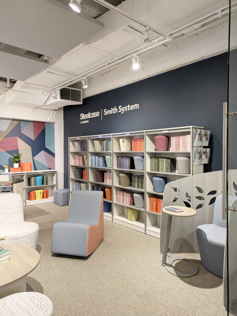A modern library room with bookshelves, colorful books, seating options, decorative partitions, and a wall labeled 