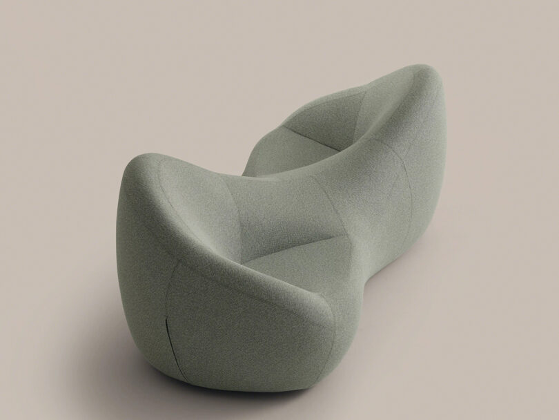 A modern, abstract light green upholstered sofa with curved, organic shapes is set against a plain beige background.