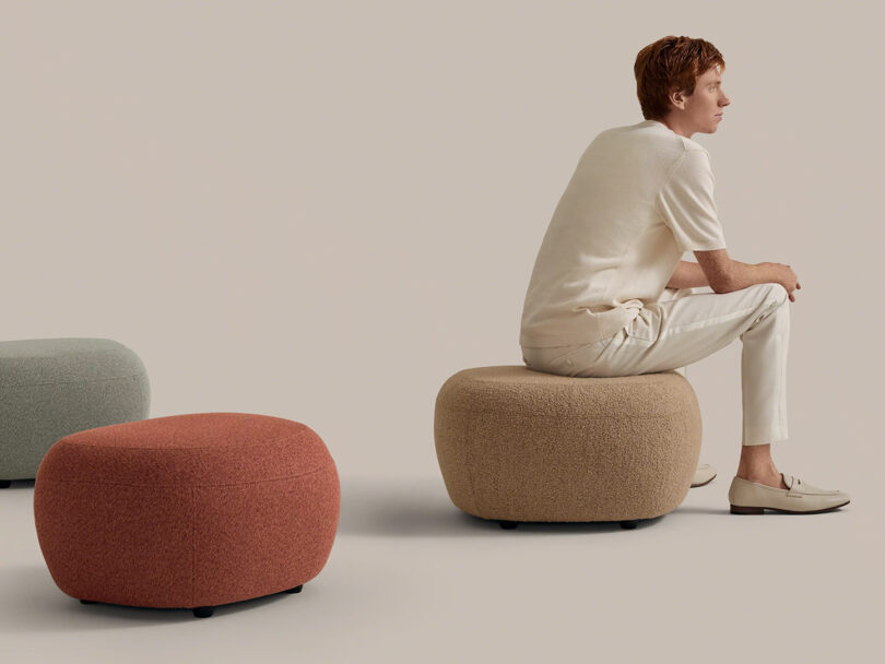 A person in light clothing sits on a beige round ottoman, with two other ottomans—one red and one green—nearby, against a plain background.
