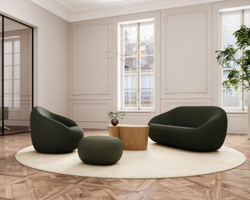 A modern living room with green armchairs, an ottoman, a wooden coffee table on a round rug, light walls, and large windows.