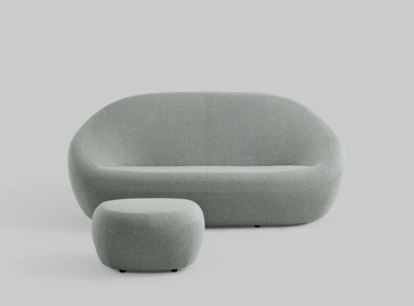 A light gray curved modern sofa by Jean Nouvel Coalesse with matching ottoman, both upholstered in fabric, placed against a plain light gray background.