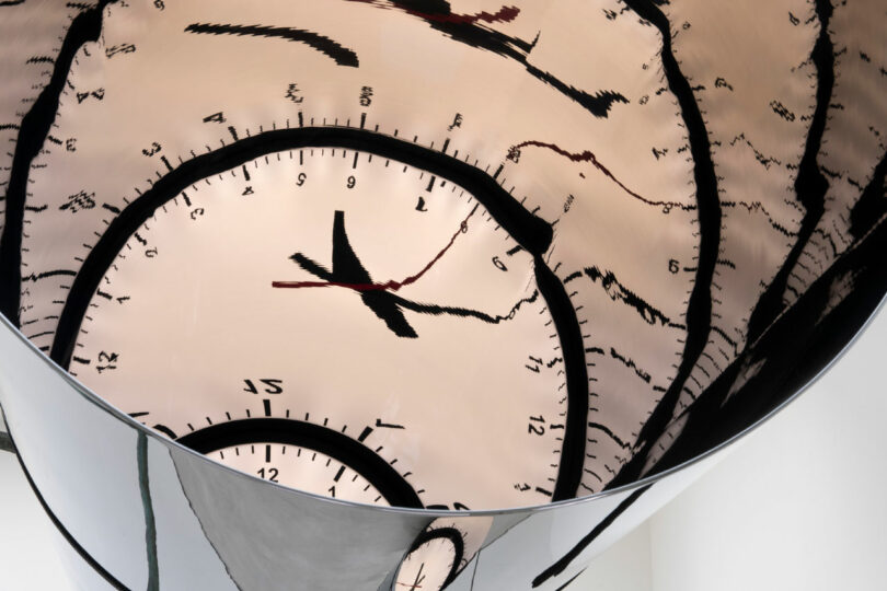 reflections of a clock in mirrored pipe