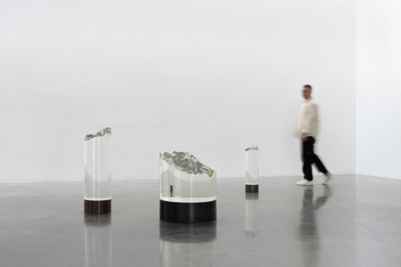 visitor walks near glass sculptures in gallery