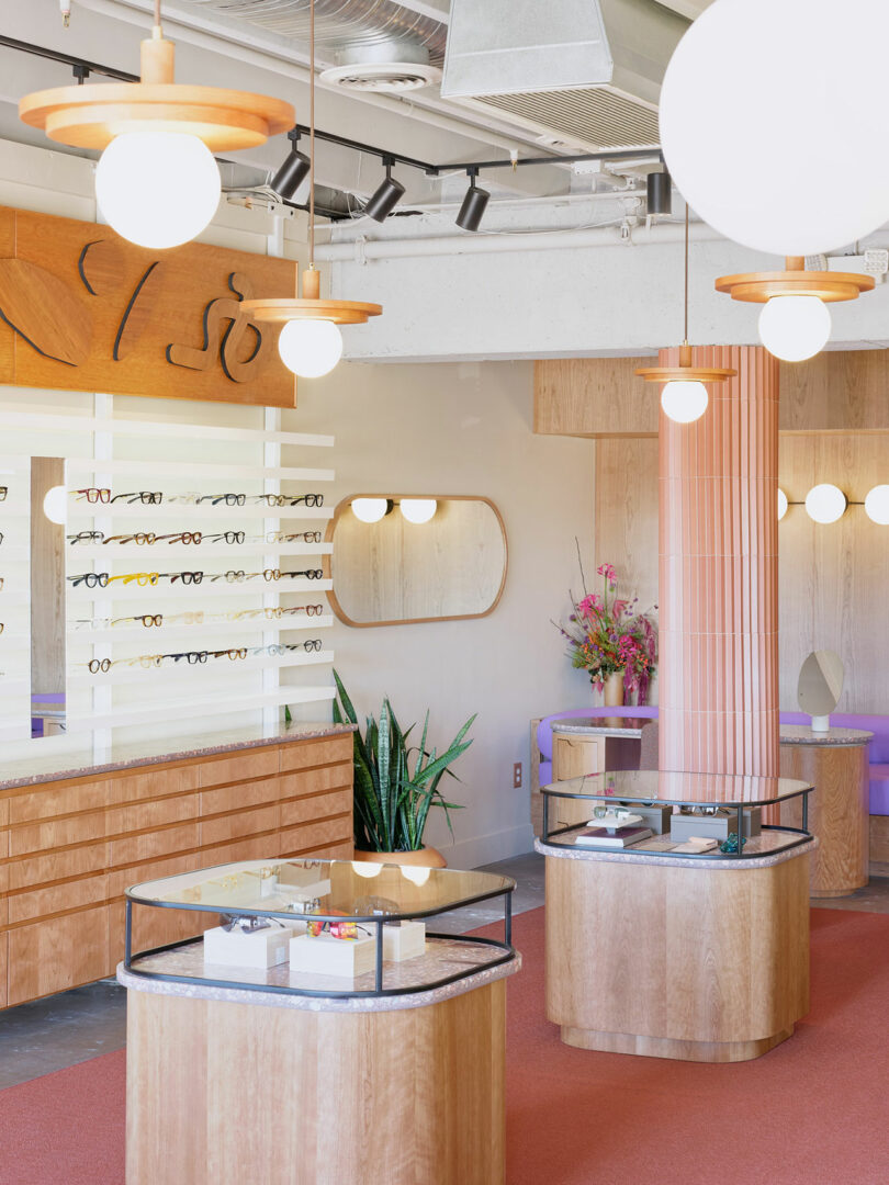A stylish eyewear store with wooden displays and shelves showcasing various eyeglasses. Modern lighting and a few plants add to the decor.