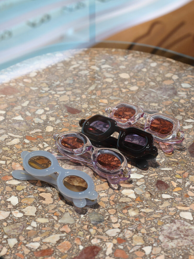 Four pairs of stylish sunglasses in various colors rest on a terrazzo table, capturing sunlight.