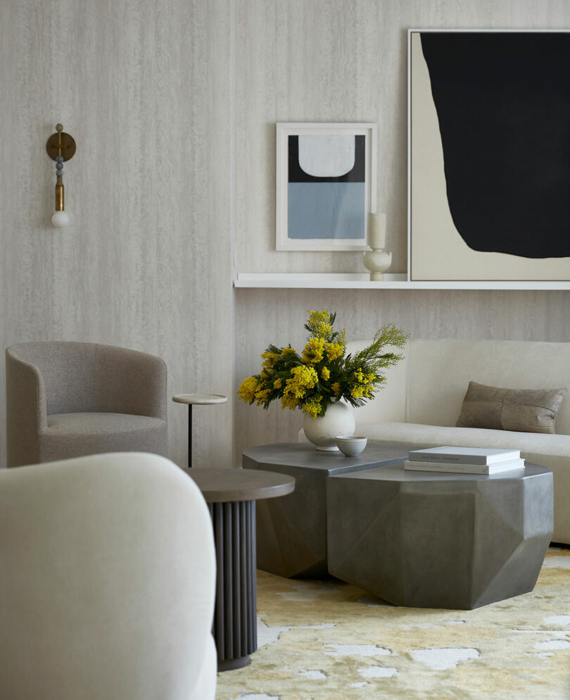 A modern living room with neutral-toned furniture, abstract art on the wall, geometric coffee tables, and a vase of yellow flowers on the table, inspired by Tina Ramchandani’s signature design style.
