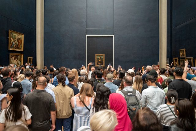 France-Hikes-Museum-Ticket-Prices-for-Non-European-Tourists.jpg A crowd of people before a painting.