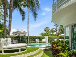 The facade of a home and a swimming pool surrounded by palm trees.
