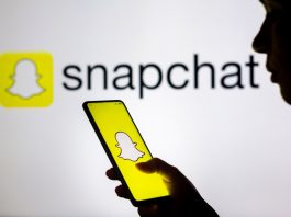 In this photo illustration, a woman's silhouette holds a smartphone with the Snapchat logo displayed on the screen and in the background.