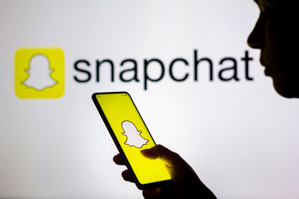 Snapchat-adds-new-features-for-creators-including-an-easier-way.jpg In this photo illustration, a woman's silhouette holds a smartphone with the Snapchat logo displayed on the screen and in the background.