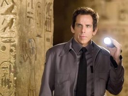 A museum guard holding a flashlight up to a wall lined with hieroglyphics.