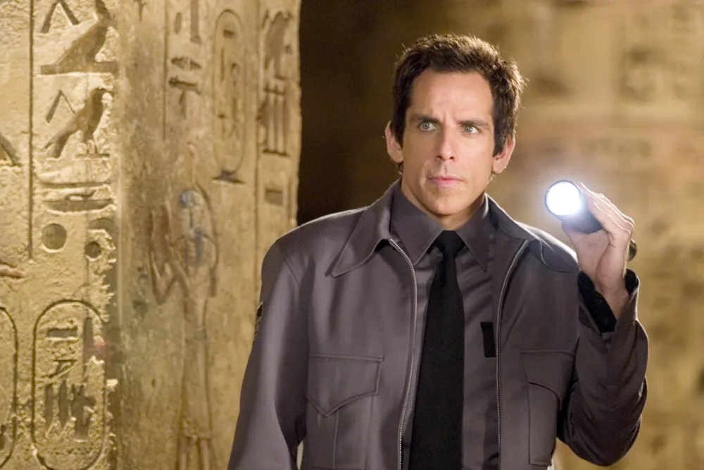 A museum guard holding a flashlight up to a wall lined with hieroglyphics.