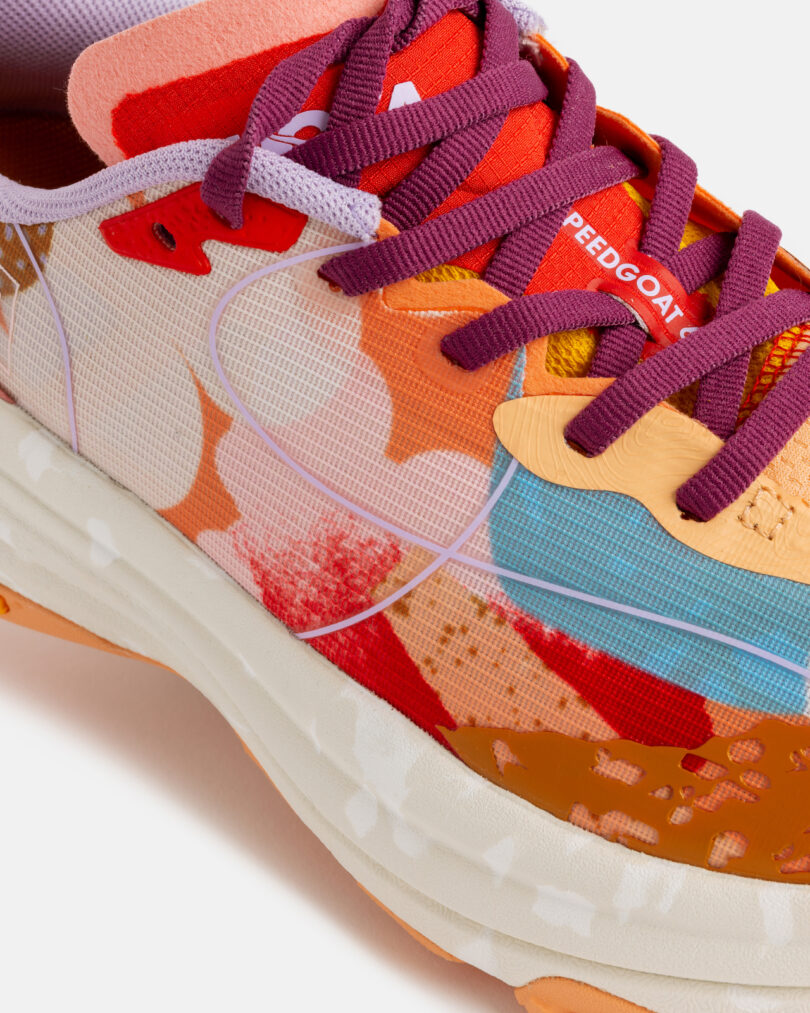 Close-up of a colorful, patterned running shoe with purple laces, orange and red overlays, and white midsole, showing the word 