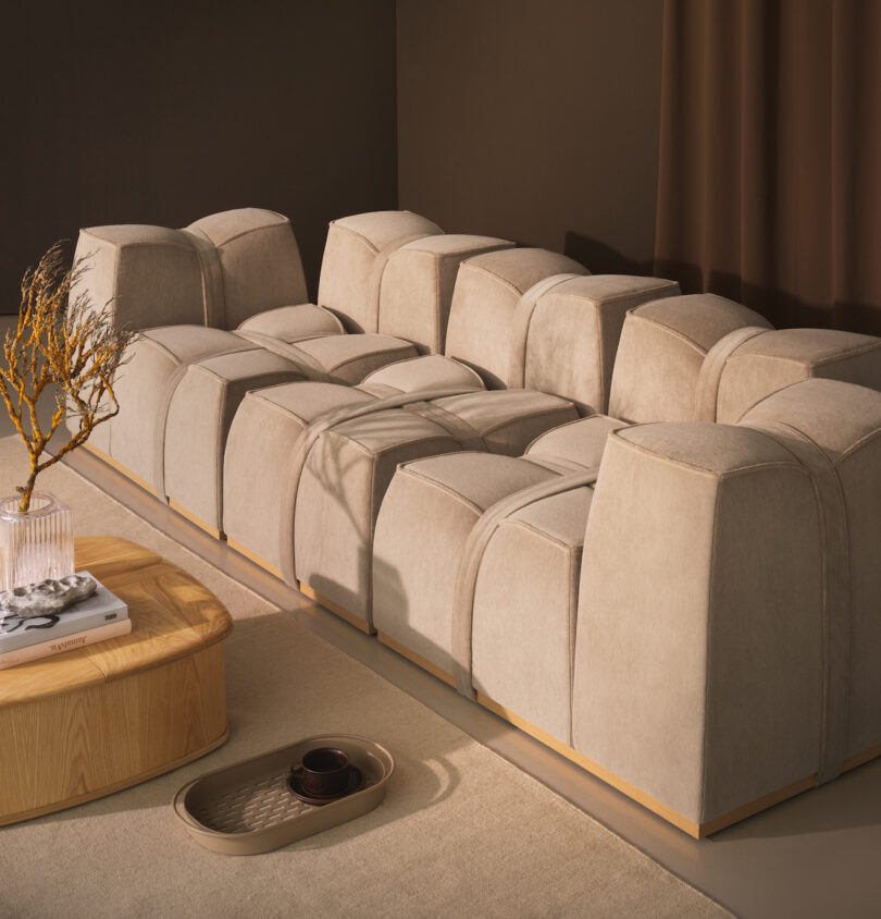 Beige modular sectional sofa with a geometric design in a modern, minimalist living room next to a light wood coffee table and neutral decor