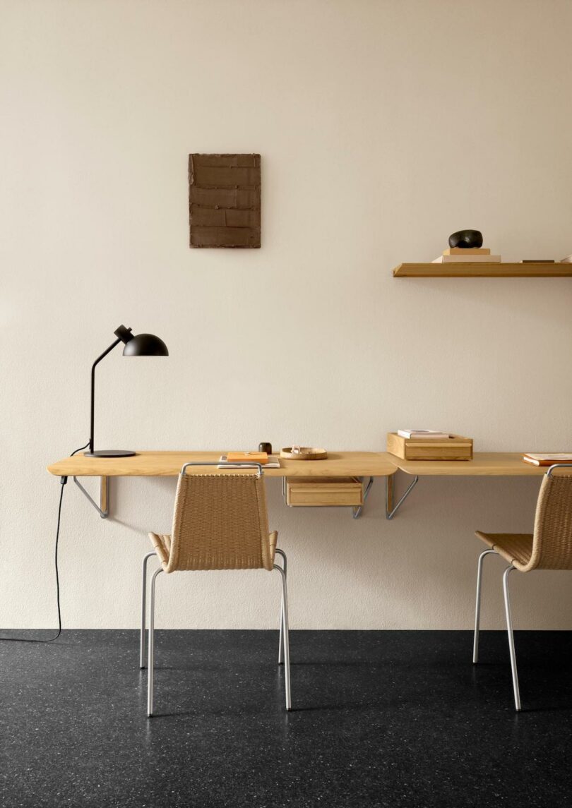 A Carl Hansen & Son woven chair sits in front of a minimalist floating black shelf with a wooden box on top, next to a cream curtain