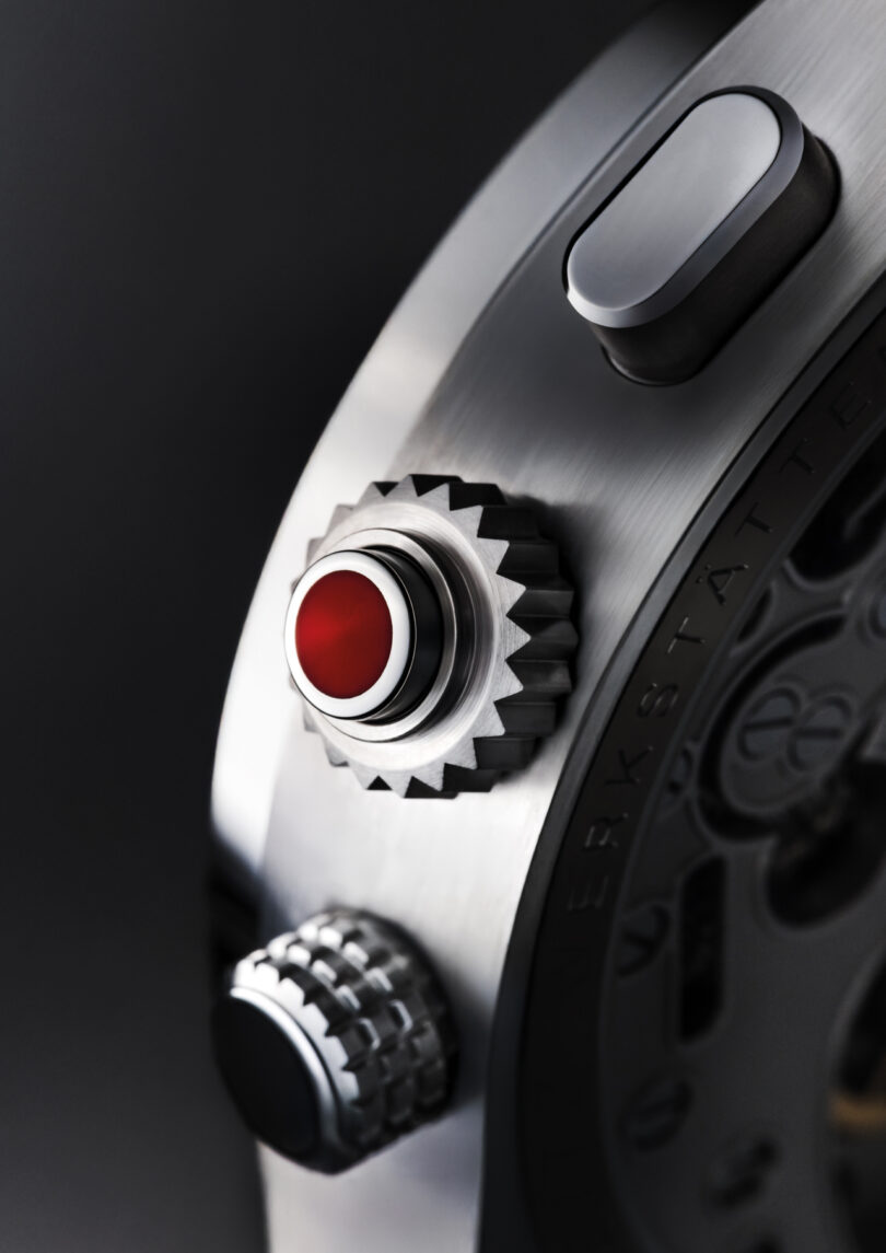 Close-up of a luxury watch reminiscent of Leica’s precision, showing a metal case, a red-capped crown, a button, and part of the mechanical movement in the background.