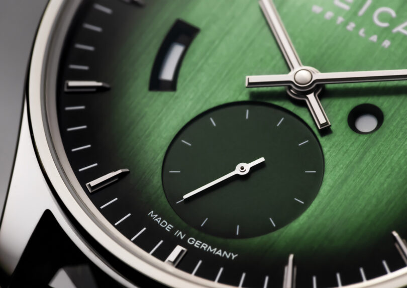 Close-up of a green Leica watch face with silver hands, a small seconds subdial, and the text 