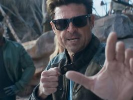 dark haired man in glasses and leather jacket raising his hands for a fight.