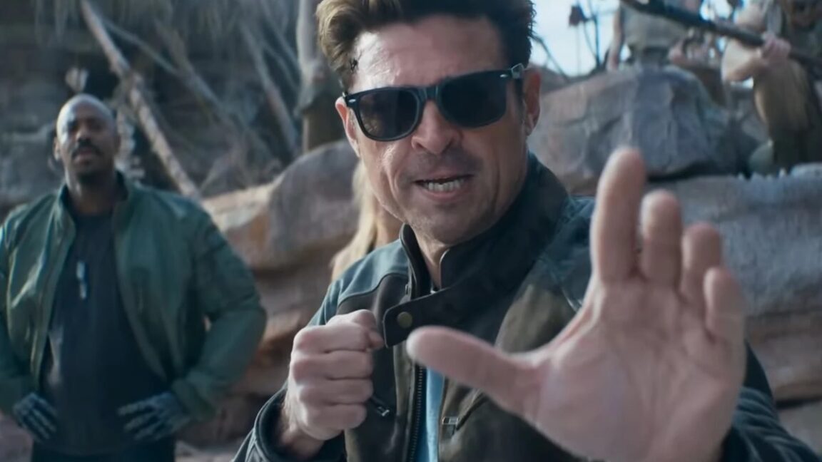 Karl-Urban-is-a-wise-cracking-Johnny-Cage-in-Mortal-Kombat.jpg dark haired man in glasses and leather jacket raising his hands for a fight.