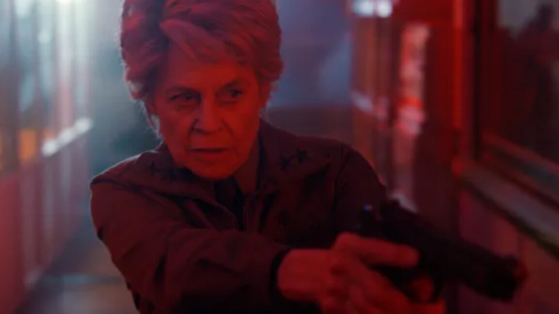 older woman with short gray hair looking grim while pointing a revolver