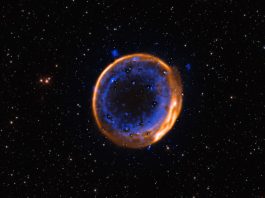 Image of a dark background punctuated with stars, with a bright ring in the center that is comprised of an outer orange and inner blue ring.