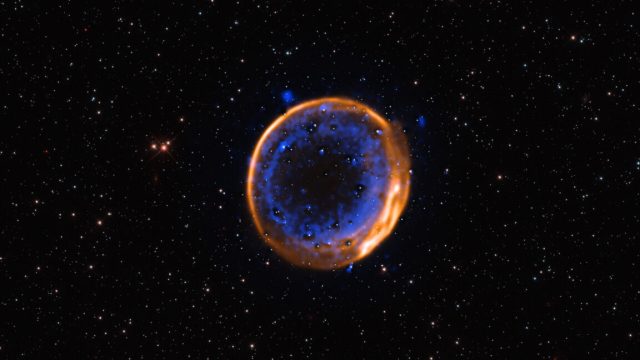 New-evidence-that-some-supernovae-may-be-a-double-detonation.jpeg Image of a dark background punctuated with stars, with a bright ring in the center that is comprised of an outer orange and inner blue ring.