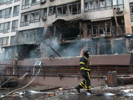 A burning building with smoke and a man in a black and yellow protective suit.
