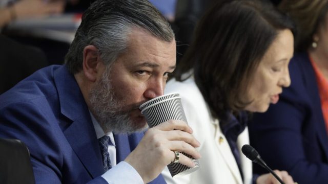 Sen. Ted Cruz drinks from a cup during a Senate committee hearing. Sen. Maria Cantwell sits next to him.